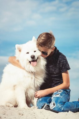 Mutlu 11 yaşında bir çocuk ile oynarken onun köpek doğurmak Samoyed, deniz kıyısı mavi gökyüzü karşı kapatın. Arkadaşlar diğer en iyi ve eğlenceli tatile, kuma oyun