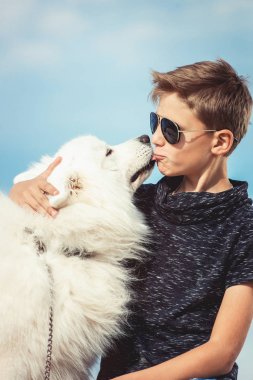 Mutlu 11 yaşında bir çocuk ile oynarken onun köpek doğurmak Samoyed, deniz kıyısı mavi gökyüzü karşı kapatın. Arkadaşlar diğer en iyi ve eğlenceli tatile, kuma oyun