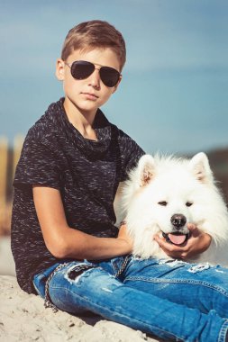 Onun köpek doğurmak Samoyed, deniz kıyısı mavi gökyüzü karşı yakın çekim sarılma mutlu 11 yaşında bir çocuk. dinlenmek ve eğlenmek tatil, kuma oyun