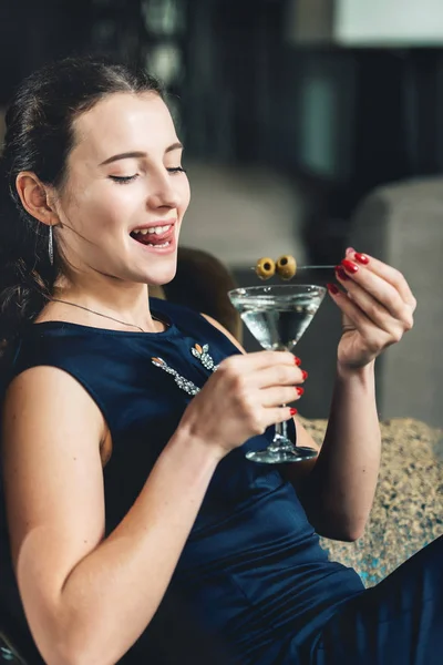 Fashionable gorgeous girl in a dark blue dress drinking cocktail in a luxery hotel lobby bar — Stock Photo, Image