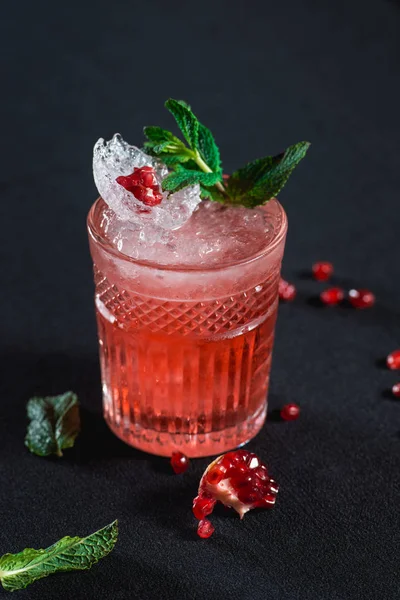 Cocktail frio com sementes de gelo e granada, pedaço de romã atrás no fundo escuro — Fotografia de Stock
