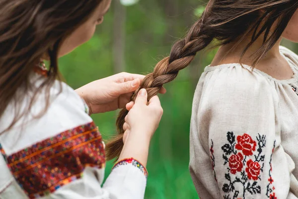Concepto de ocio femenino. Hermanas, mejores amigas en ropa tradicional ucraniana haciendo trenzas, se peinan — Foto de Stock