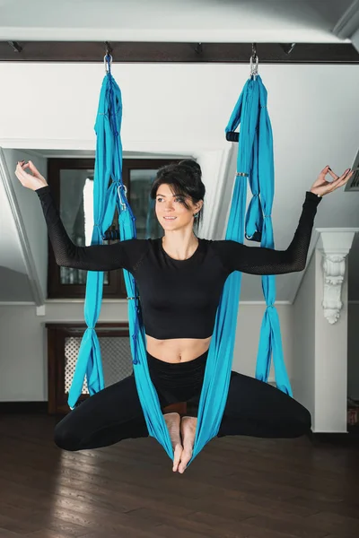 Yoga in a white room. woman performs physical exercises fly-yoga, pilates on a special equipment