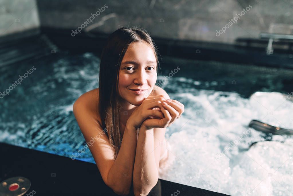 Sexy beautiful caucasian woman relaxing in a pool with jacuzzi. Dark room. Poor lighting.