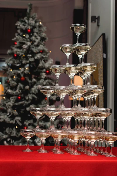 Champagne tower on a red table with Christmas tree in the background