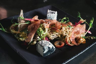 Bir taş tabakta prosciutto, domates, marul ve mavi peynir ile taze salata