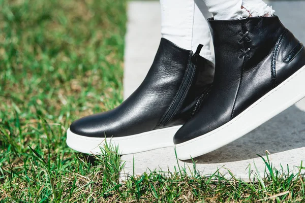Side View Of Woman's Black Leather Ankle Boots. Outdoor Shot Over White Stone in park