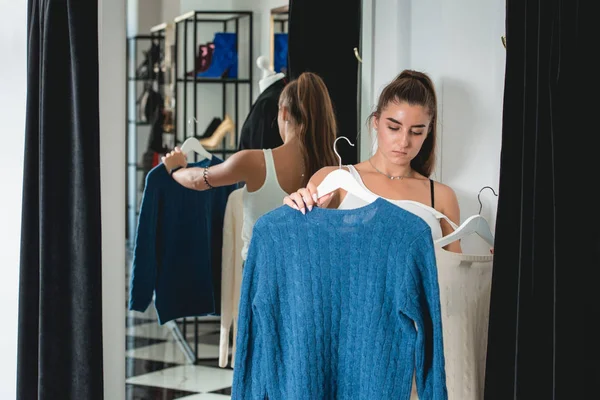 Jeune belle femme faisant du shopping, aller à la salle d'essayage dans le centre commercial de mode, prendre une décision sur ce qu'il faut acheter, tenant deux cintres avec des robes différentes, en essayant de choisir entre de nouveaux vêtements — Photo