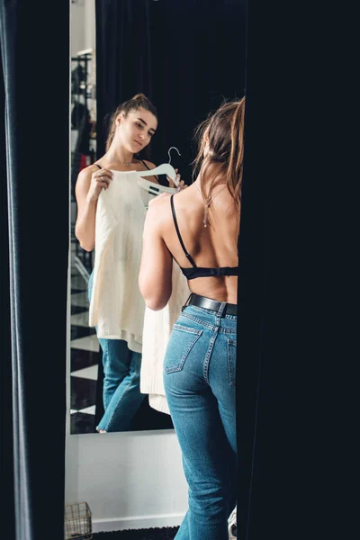 Young beautiful woman shopping, in a fitting room in fashion mall, trying on a white sweater — 스톡 사진