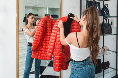 Blu jeance beyaz tişörtlü genç bir kadın lüks bir butikte kırmızı önlük deniyor.