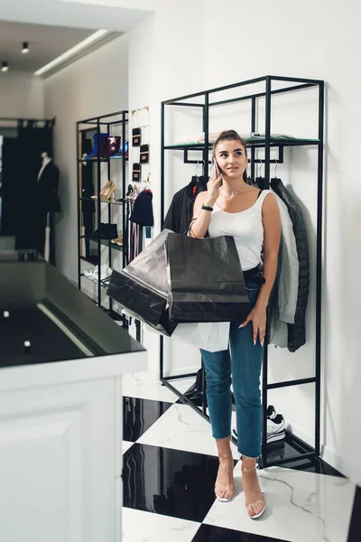 Chica sonriente haciendo muchas compras en la tienda de ropa. Mujer con paquetes en las manos en una boutique de ropa —  Fotos de Stock