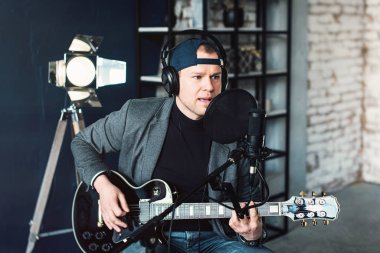 Bir ev stüdyosunda bir parça kayıt gitar ile kulaklık bir taburede oturan bir adam şarkıcı yakın