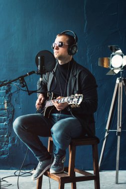 Bir ev stüdyosunda bir parça kayıt gitar ile kulaklık bir taburede oturan bir adam şarkıcı yakın