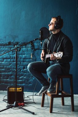 Bir ev stüdyosunda bir parça kayıt gitar ile kulaklık bir taburede oturan bir adam şarkıcı yakın