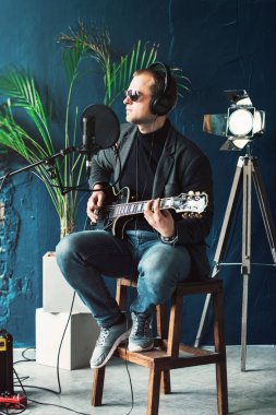 Bir ev stüdyosunda bir parça kayıt gitar ile kulaklık bir taburede oturan bir adam şarkıcı yakın