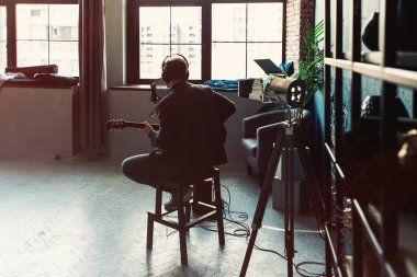Bir ev stüdyosunda bir parça kayıt bir gitar ile kulaklık bir taburede oturan adam şarkıcı