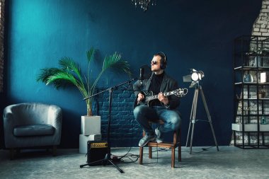 Bir ev stüdyosunda bir parça kayıt bir gitar ile kulaklık bir taburede oturan adam şarkıcı