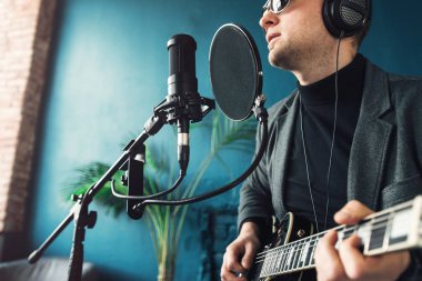 Bir ev stüdyosunda bir parça kayıt gitar ile kulaklık bir taburede oturan bir adam şarkıcı yakın