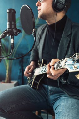 Bir ev stüdyosunda bir parça kayıt gitar ile kulaklık bir taburede oturan bir adam şarkıcı yakın