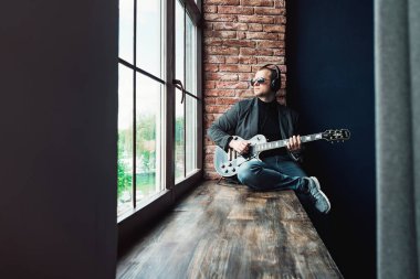 Bir ev stüdyosunda bir parça kayıt bir gitar ile kulaklık bir pencere eşik üzerinde oturan adam şarkıcı