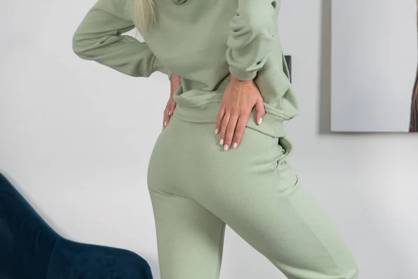 Elegante hermosa mujer rubia joven en un chándal verde posa cerca de una pared blanca en la habitación. — Foto de Stock