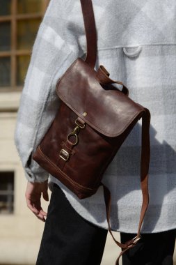 Arka planda şık bir model, klasik bir kahverengi deri sırt çantası ve şehir arka planına karşı modaya uygun bir ekose bluz sergiliyor..