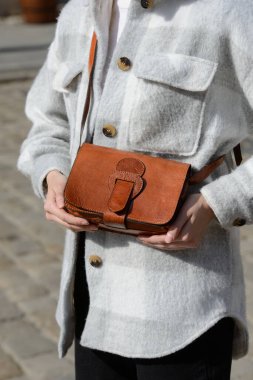 Ekose gömlekli şık bir model, küçük, kırmızımsı kahverengi deri bir çanta taşır. Eşsiz bir kapağı ve geniş bir tokası vardır. Sıradan bir zarafet sergiler.