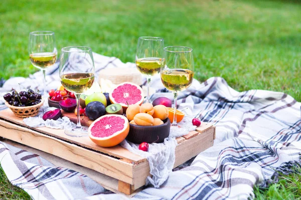 Picnic background with white wine and summer fruits on green grass
