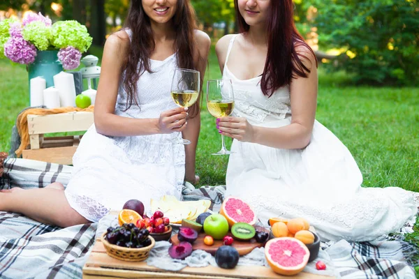Happy girlfriends with white wine on summer party in park on picnic