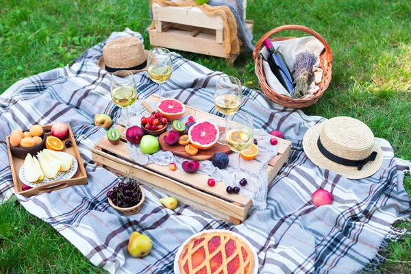 Picnic background with white wine and summer fruits on green grass