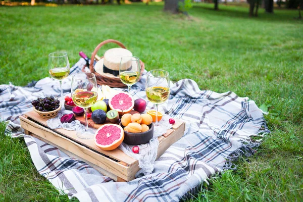 Picnic background with white wine and summer fruits on green grass