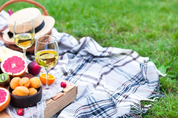 Picnic background with white wine and summer fruits on green grass