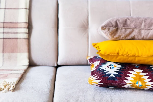 Cushions and plaid on the beige sofa close up with copy space. Sweet home and cozy concept. Indoors