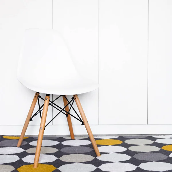 White modern designer chair in front of a white wall on the carpet, copy space, close up