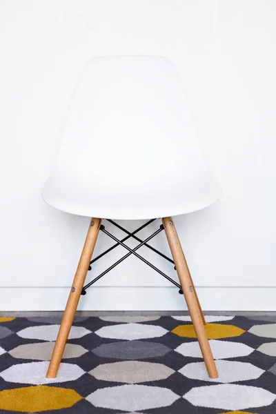 White modern designer chair in front of a white wall on the carpet, copy space, close up