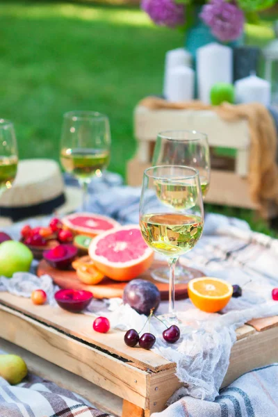 Picnic background with white wine and summer fruits on green grass