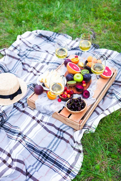 Picnic background with white wine and summer fruits on green grass