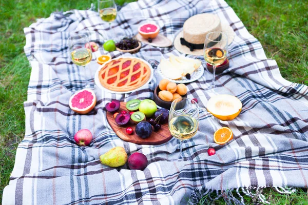 Picnic background with white wine and summer fruits on green grass