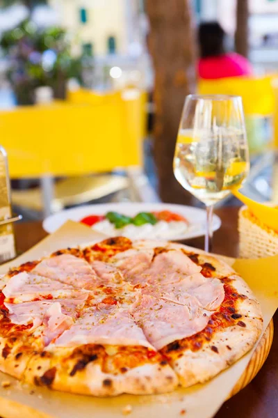 Italian food dinner. Pizza with tomato prosciutto mozzarella and glass white wine summer outdoor restaurant, selective focus