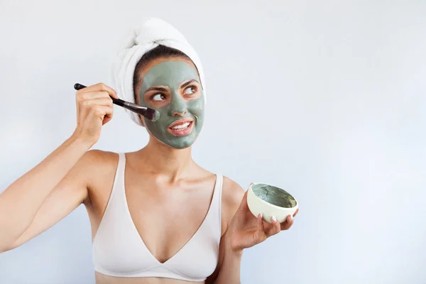 Young beautiful woman in face mask of therapeutic blue mud. Spa treatment, self care and healthy skin. Copy space, white background