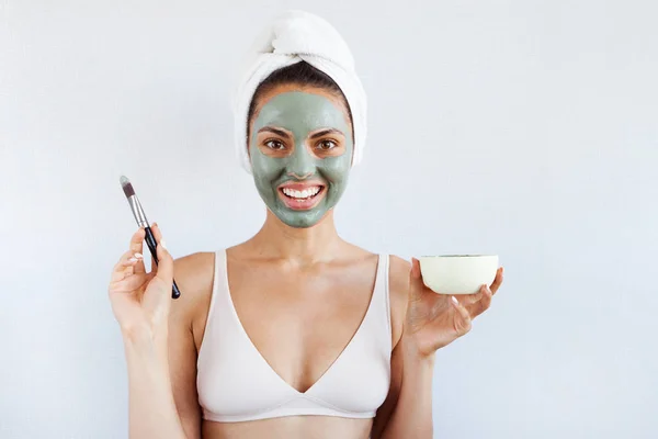 Young beautiful woman in face mask of therapeutic blue mud. Spa treatment, self care and healthy skin. Copy space, white background