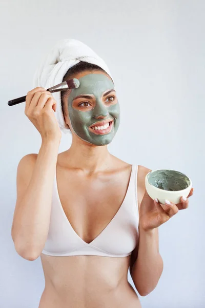 Young beautiful woman in face mask of therapeutic blue mud. Spa treatment, self care and healthy skin. Copy space, white background