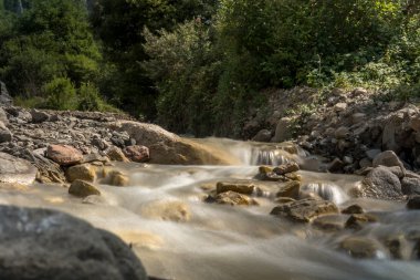 Dağ nehir hızlı akış ve parlak bulanık dalgalar ile. Temiz su içinde büyük yosunlu kayalar.