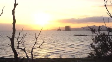 Harika deniz manzaralı ağaçlar siluet çerçeve kenarlığı yapma. Dağ ve petrol derrick ile deniz kıyısı. 4k video.