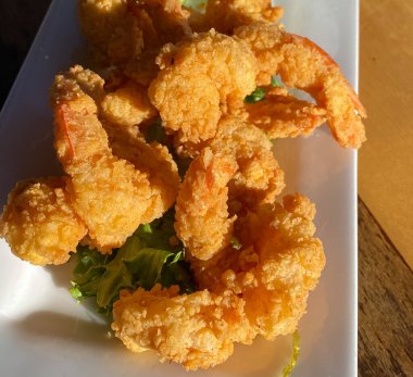 Güneş altında beyaz bir porselen tabakta kızartılmış karidesin yakın görüntüsü.