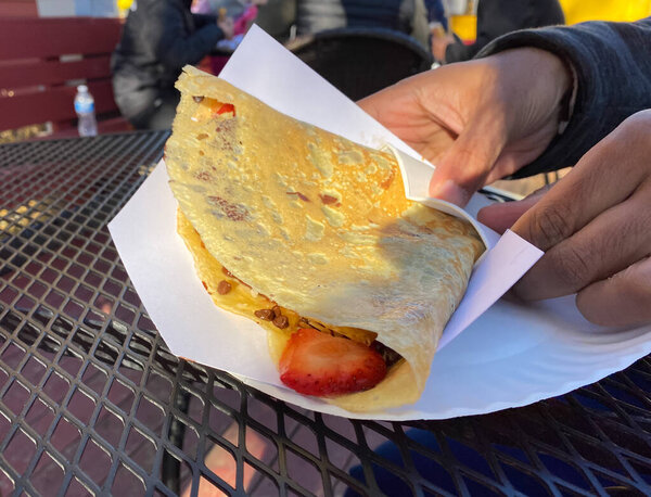Customer hand holds a sweet crepe in the crepes a la cart restaurant
