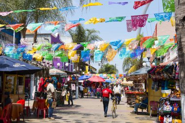 Tijuana, Baja California'deki/Meksika - 20 Haziran 2018: İnsanlar dükkan Plaza Santa Cecilia, şehrin göbeğinde tarihi bir Meksikalı meydanda, renkli asılı bayrakları altında.
