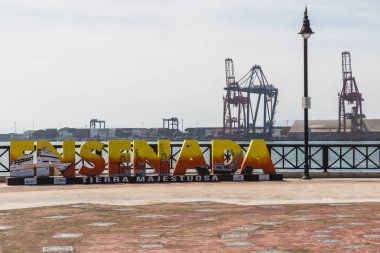 ENSENADA, MEXICO - OCTOBER 22, 2018:  Giant colorful letters welcome visitors to Ensenada harbor, while a trio of Panamax cranes stand in the background.  Ensenada is the second busiest port in Mexico clipart