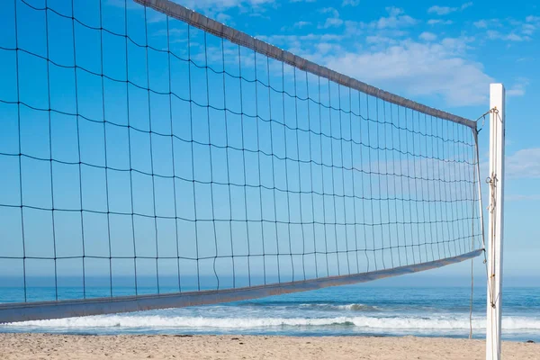 Beach volleyball net with ocean waves in the background.