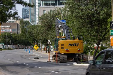 Kanada, 05 Temmuz 2025: Kazıcı, ağaçlar, işaretler ve binalarla çevrili Montreal şehir merkezinde faaliyet gösteriyor
